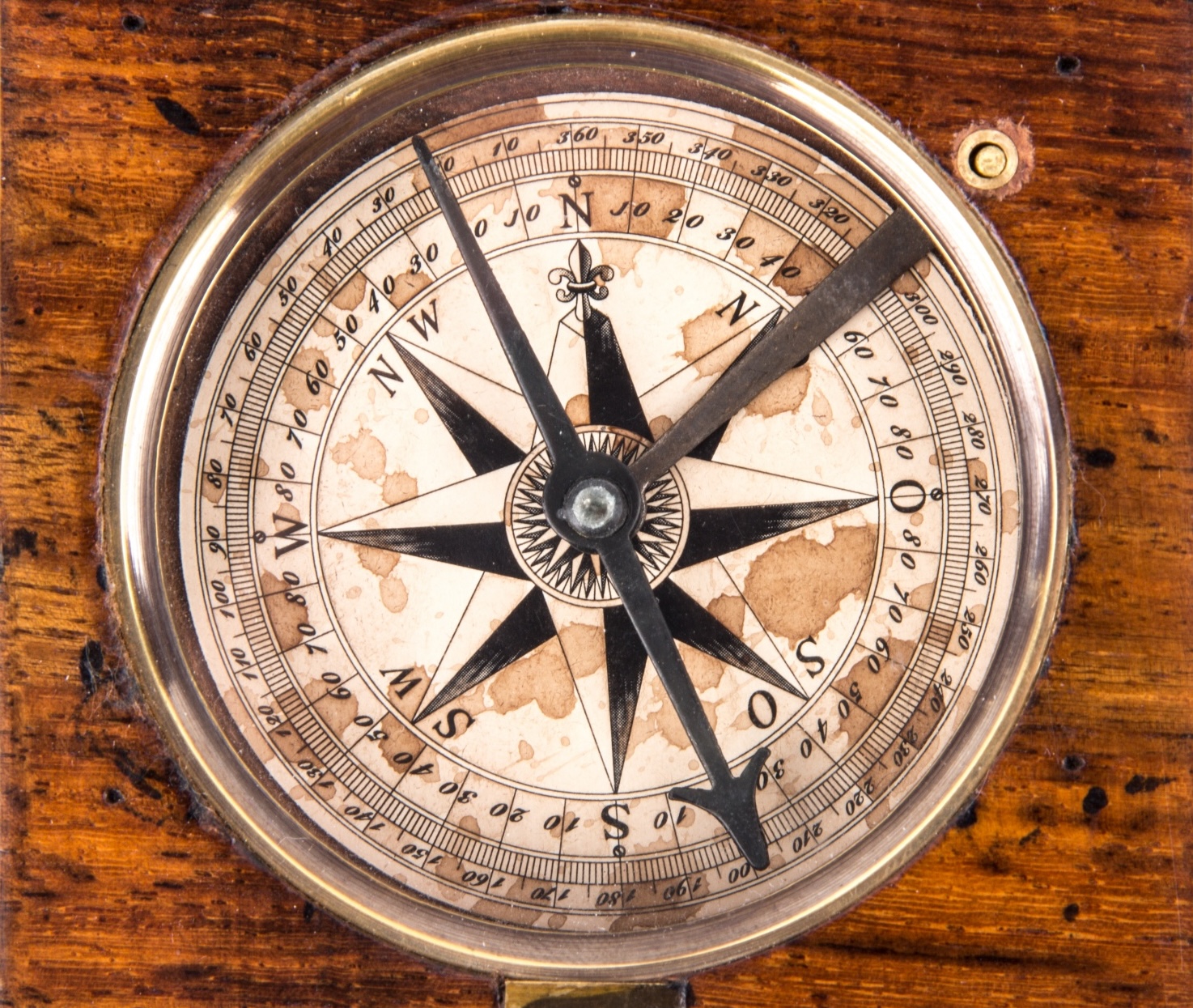 antique compass with browning water stains embedded in wooden panel
