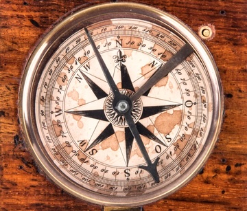 close up of the top view of an aged and weathered compass on a wooden background