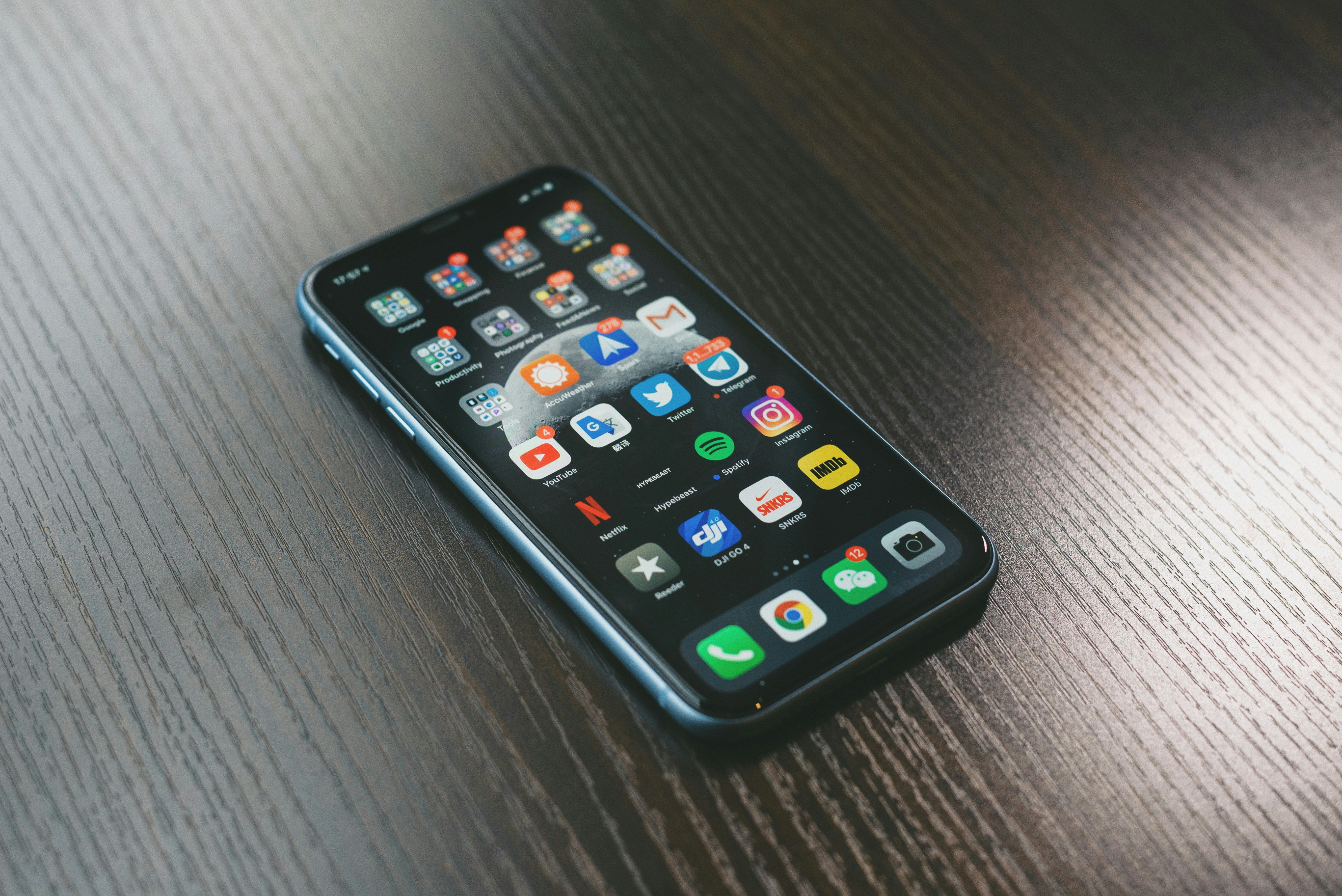 iPhone lying on a reflective yet dark wooden textured table showing iPhone apps. Credit to Jonas Lee from Unsplash.com
