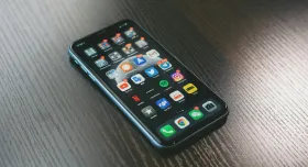 iPhone lying on a reflective yet dark wooden textured table showing iPhone apps. Credit to Jonas Lee from Unsplash.com
