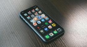 iPhone lying on a reflective yet dark wooden textured table showing iPhone apps. Credit to Jonas Lee from Unsplash.com